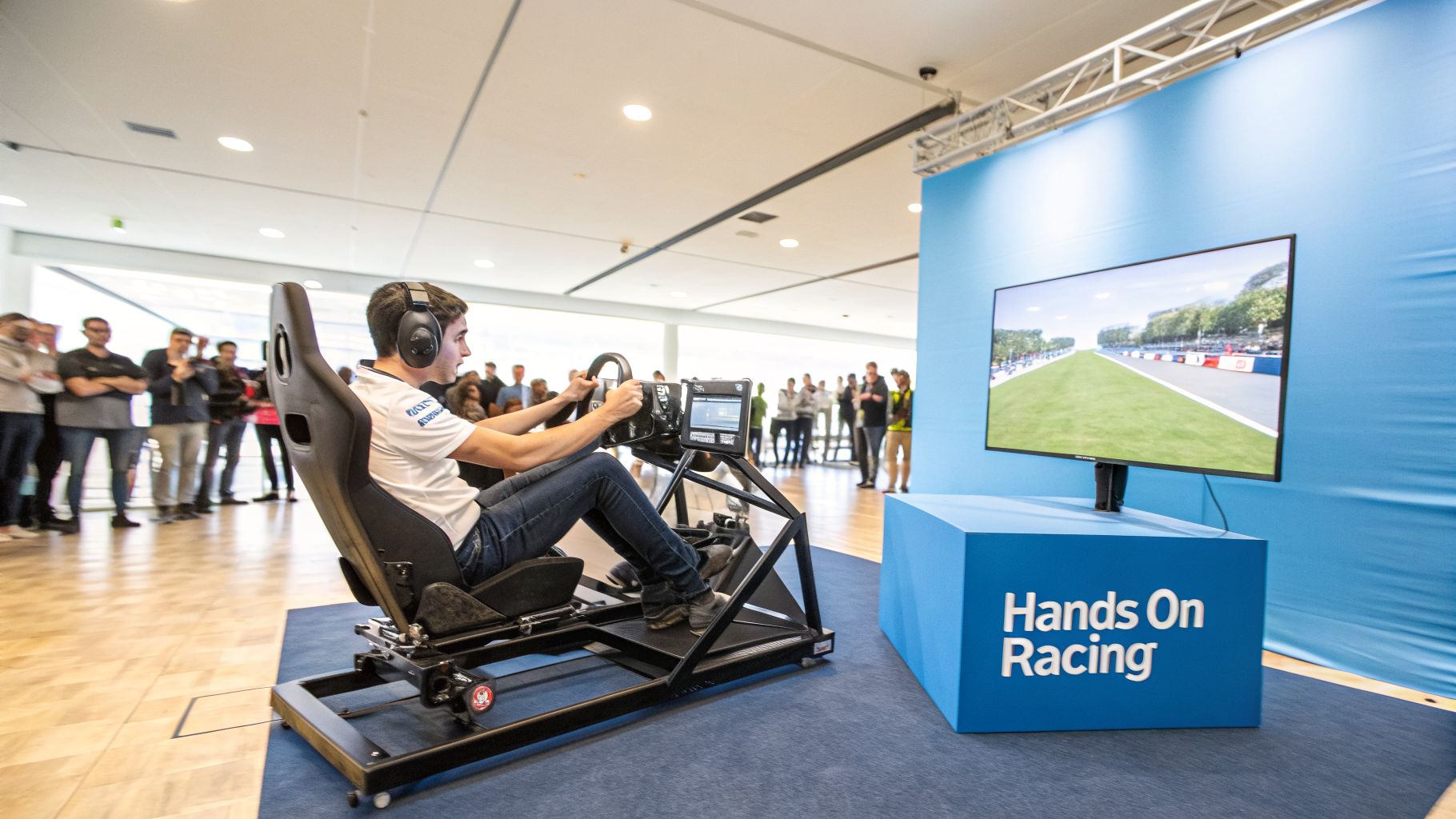 A man wearing headphones plays an online car racing simulator, steering a wheel while watching a virtual track.