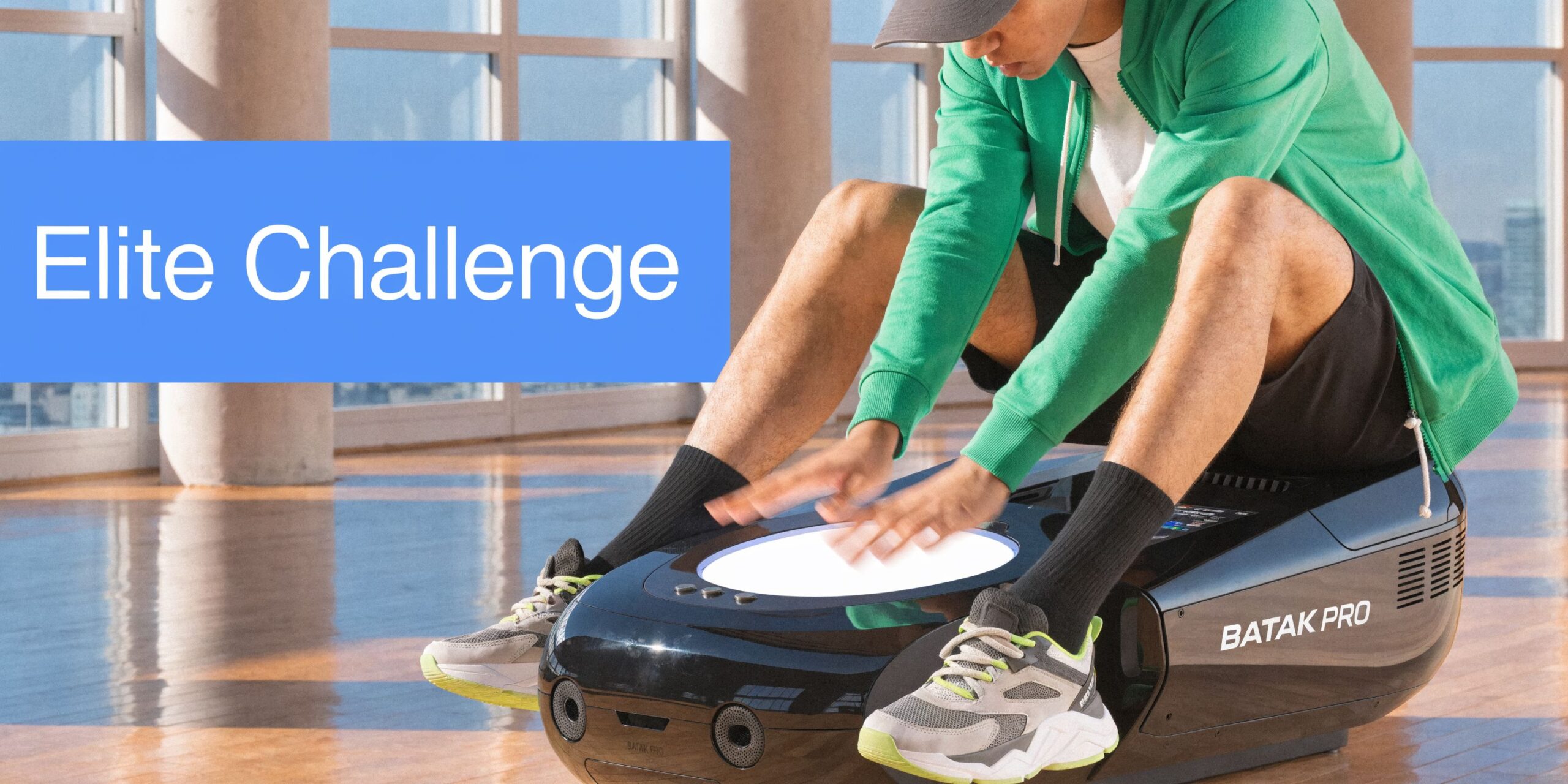 A person wearing a green hoodie sitting on a Batak Pro reaction training machine in a bright studio.