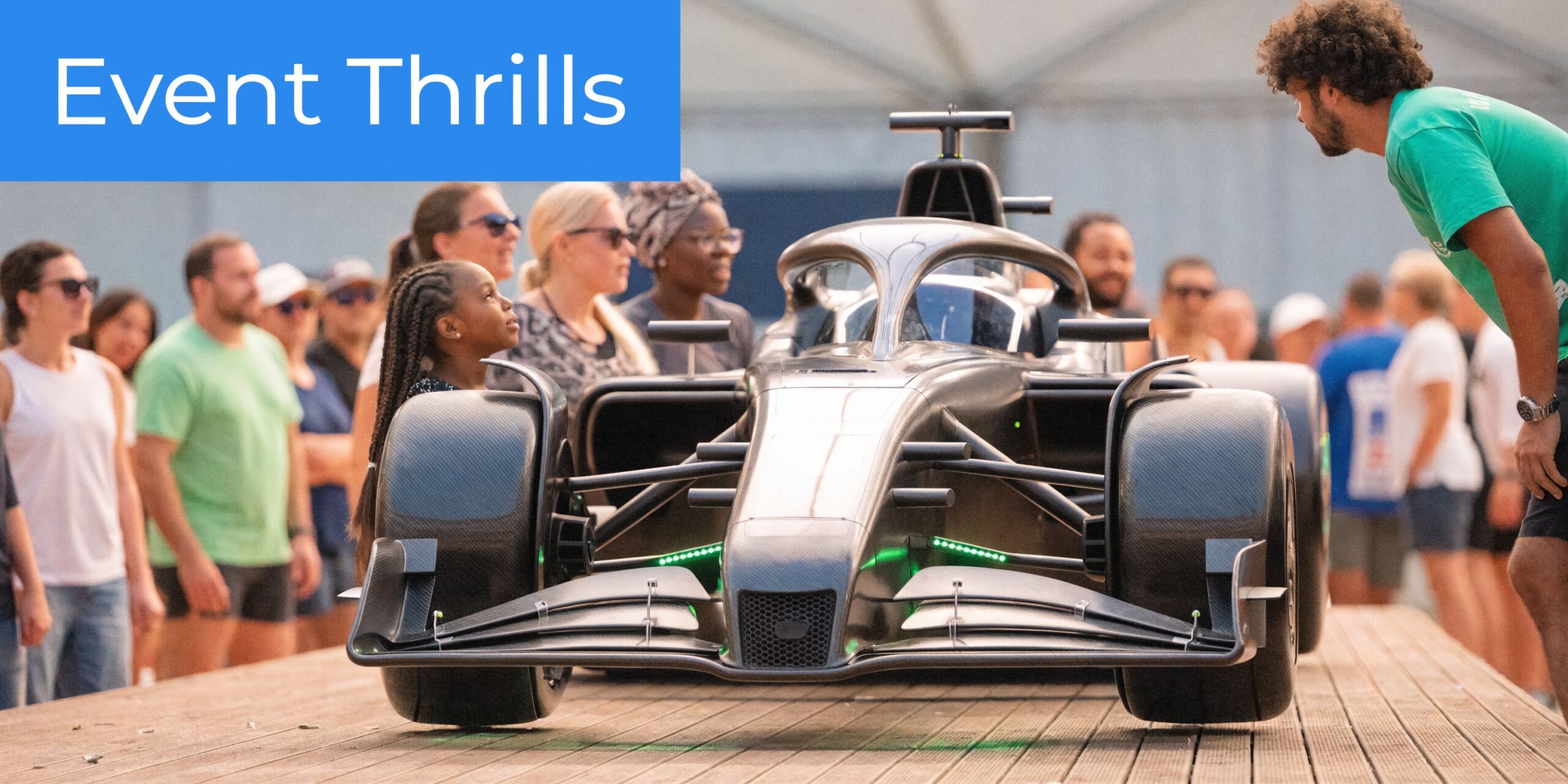 A young girl and onlookers admire a modern Formula 1 race car on display at an event.