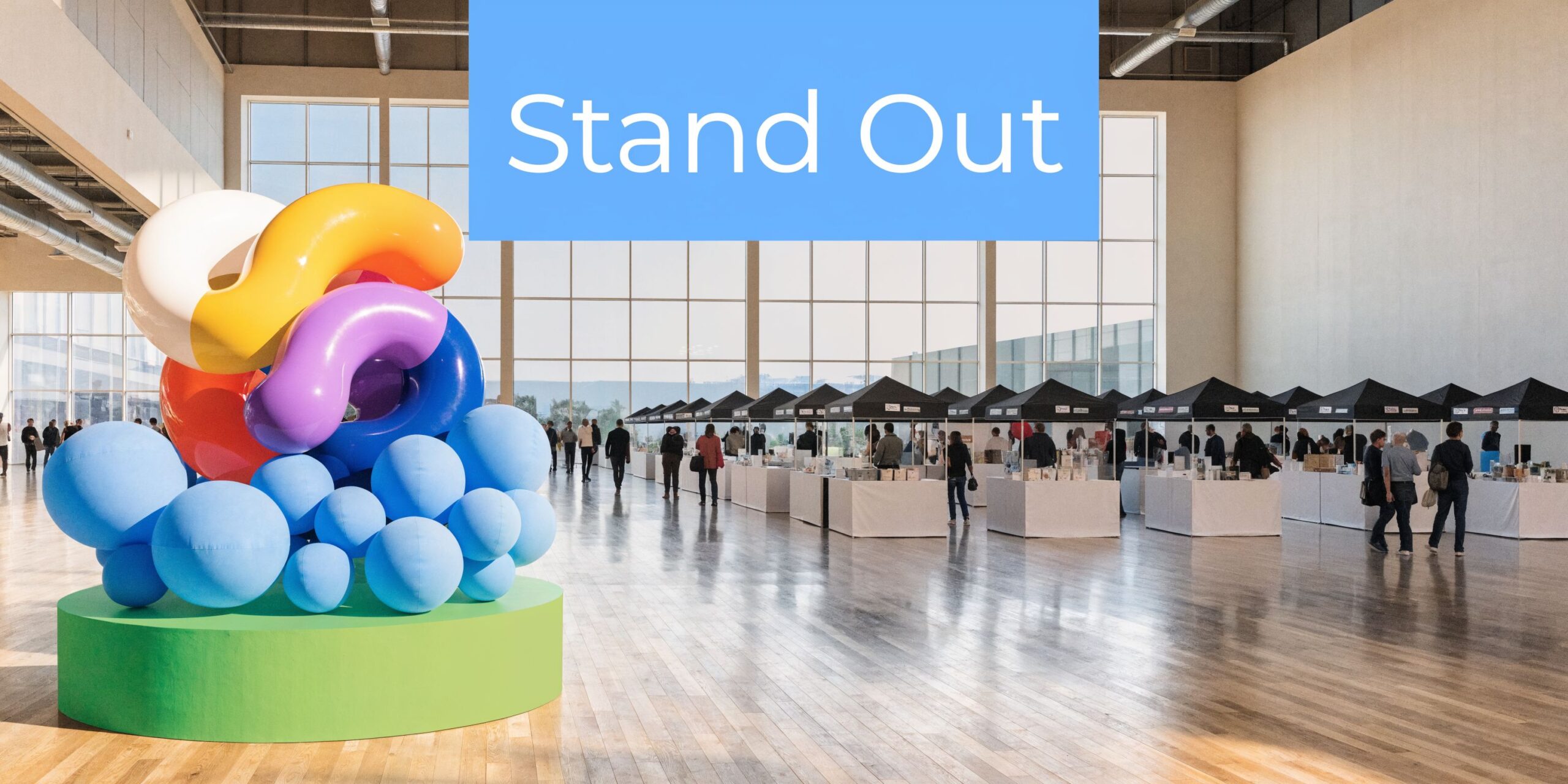 A modern exhibition hall featuring colorful abstract art sculptures and rows of professional pop-up vendor booths.