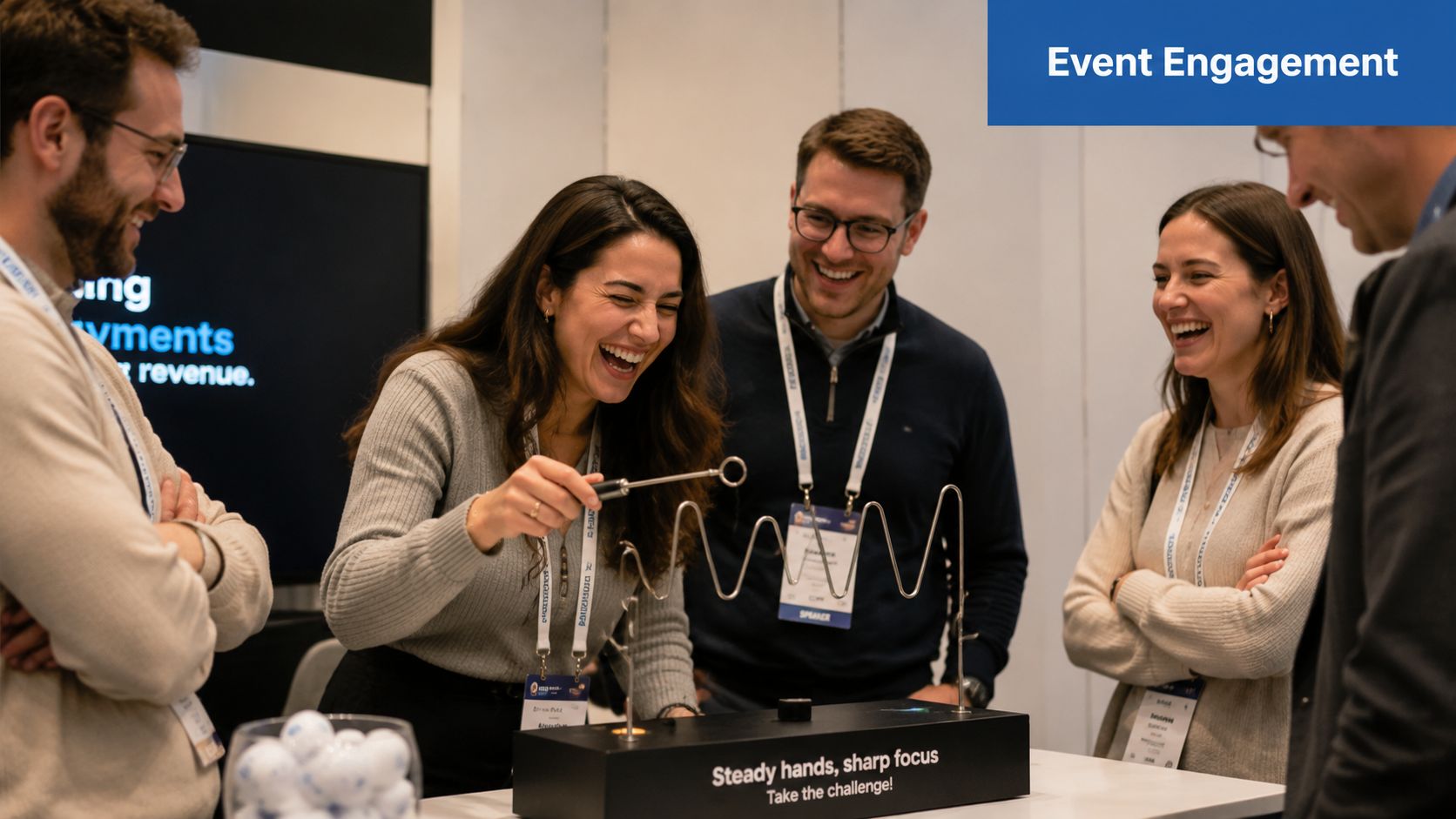 A group of colleagues laughing while playing the steady hands game at an event booth.
