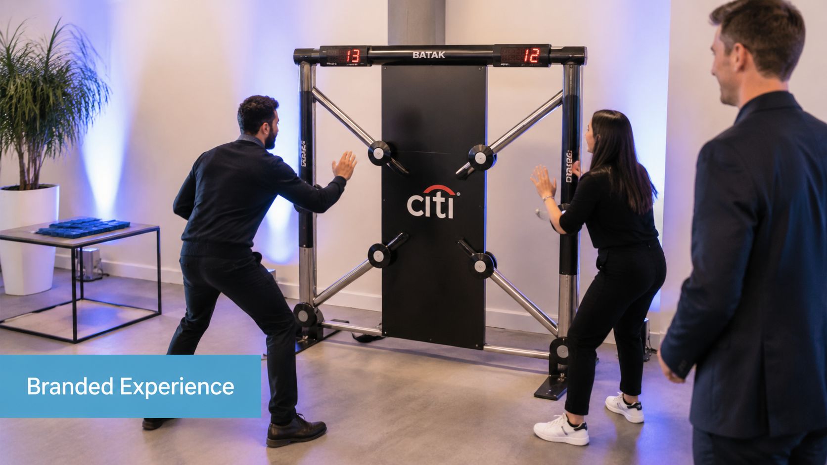 Two people competing on a Citi-branded Batak wall reaction game while a man watches in an office.