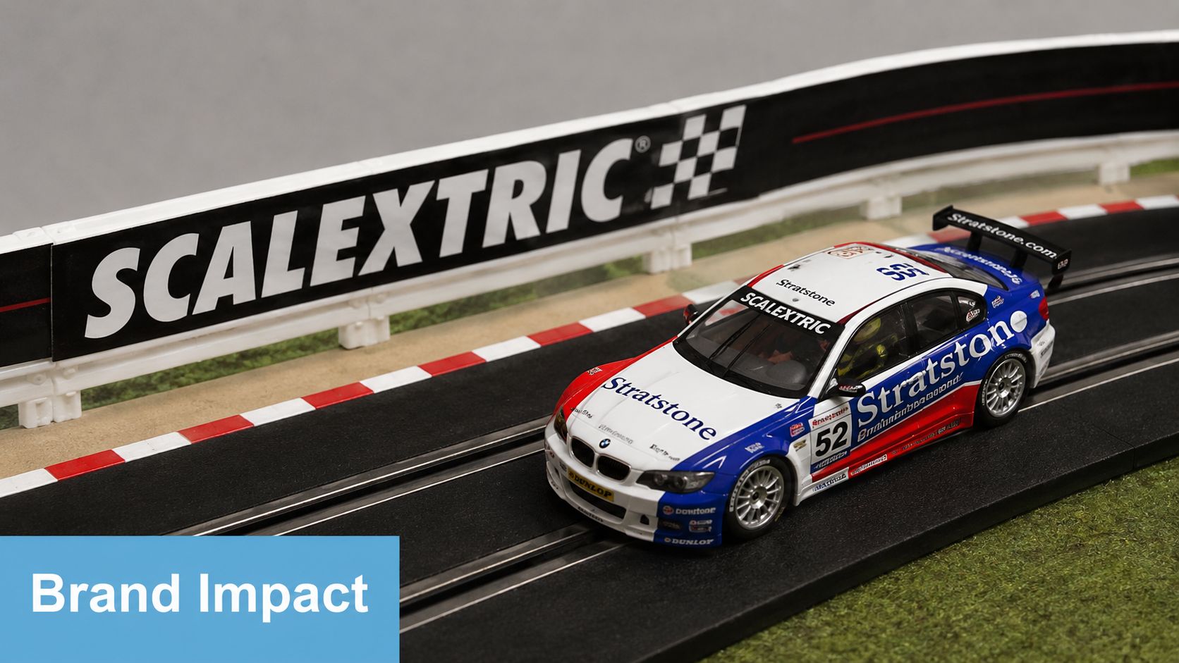 A detailed Scalextric toy race car branded with Stratstone livery driving on a miniature racetrack circuit.