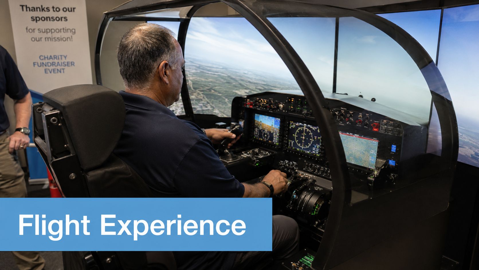 A man piloting a professional flight simulator during a charity fundraiser event at an indoor location.