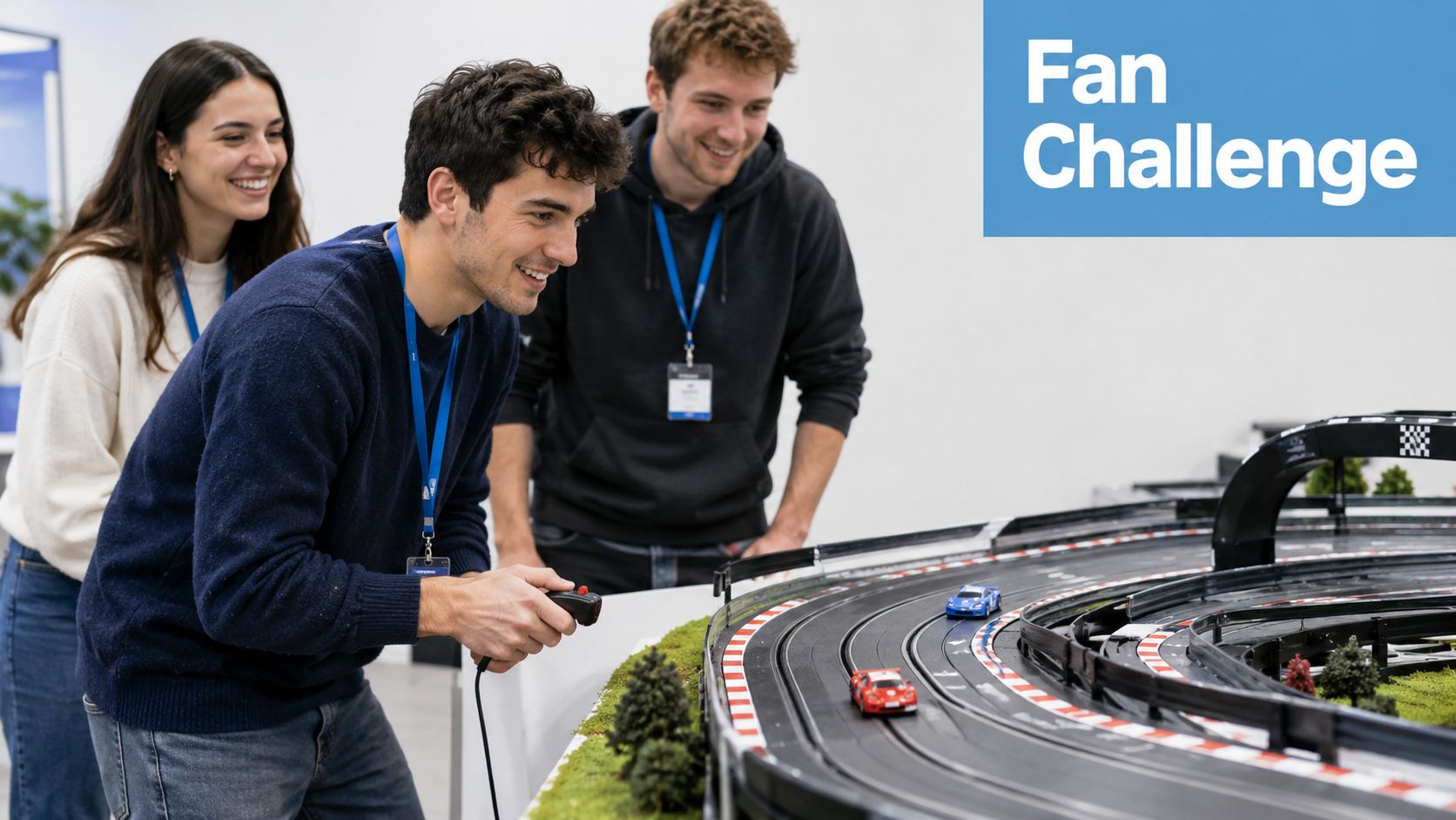 Three people smiling while watching toy cars racing on a miniature track at an event.